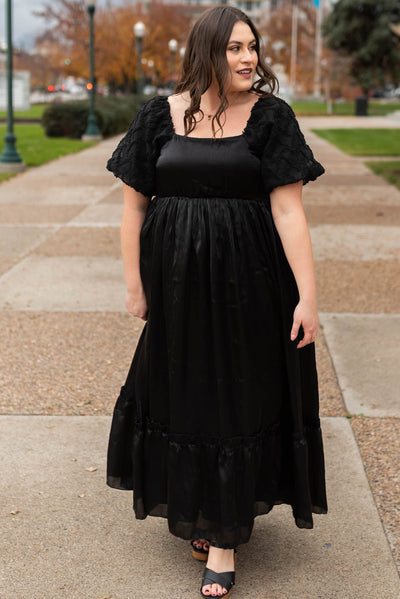Front view of a plus size black organza dress with a square neck and ruffle hem