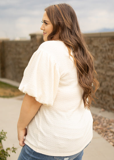 Side view of a plus size cream textured top with short puff sleeves
