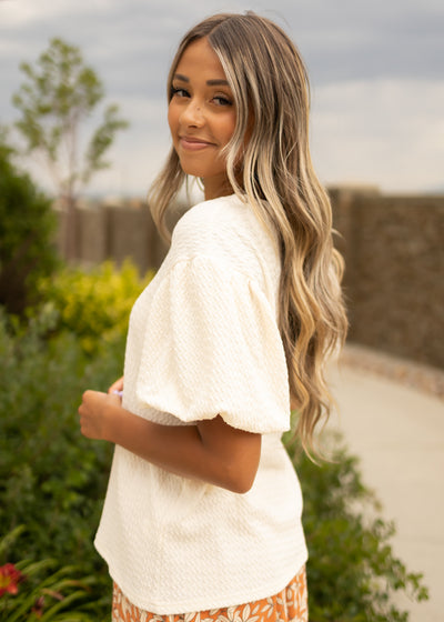 Side view of a short puff sleeve cream textured top
