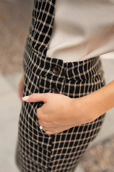 Side view of black plaid overalls with buttons at the waist