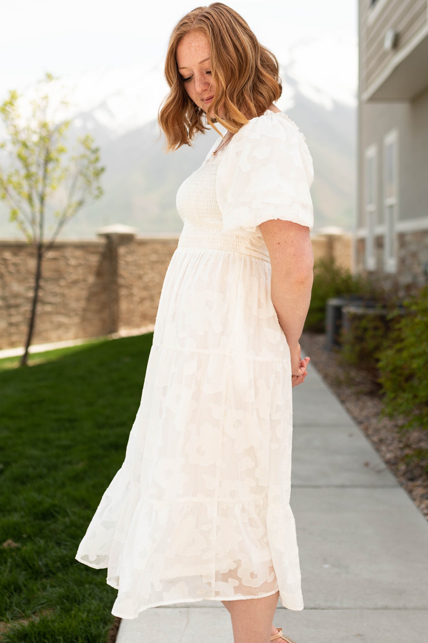 Side view of a white dress with flower print fabric, short sleeves and smocked bodice