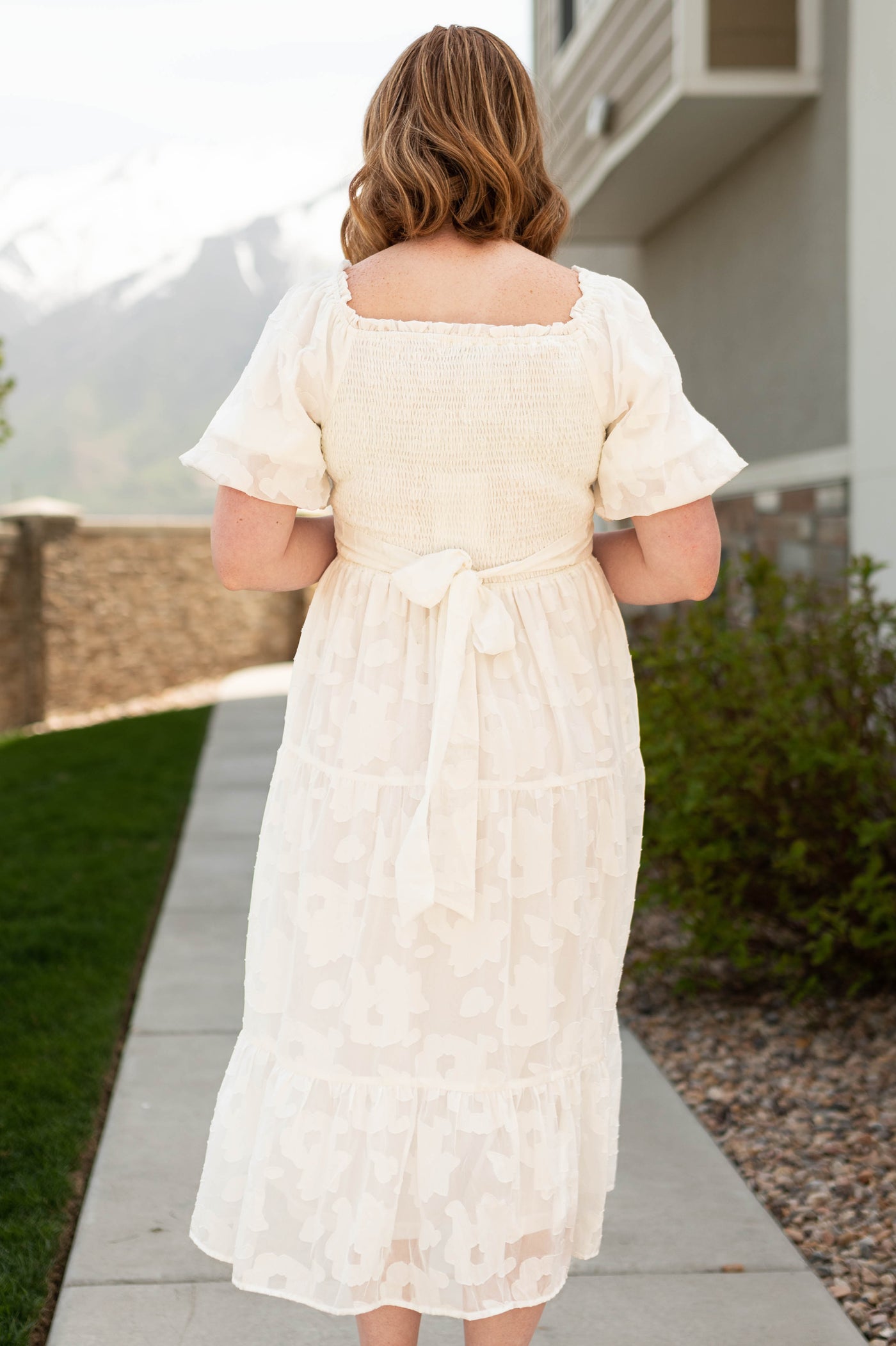 Back view of a white dress with flower print fabric, short sleeves and smocked bodice