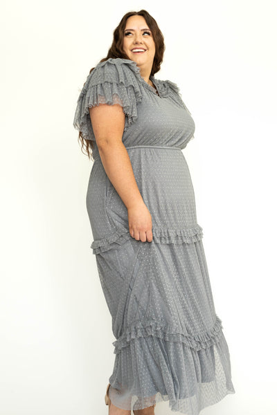 Side view of a blue gray plus size lace short sleeve dress with ruffles on sleeves and neck.