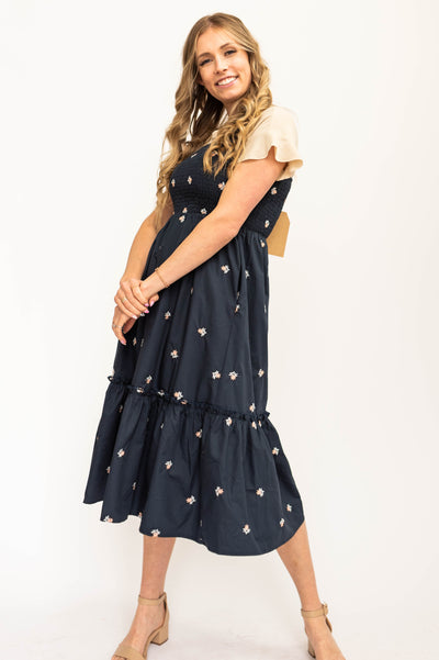 Front view of a navy sundress, elastic straps, smocked bodice with white daisy floral print.