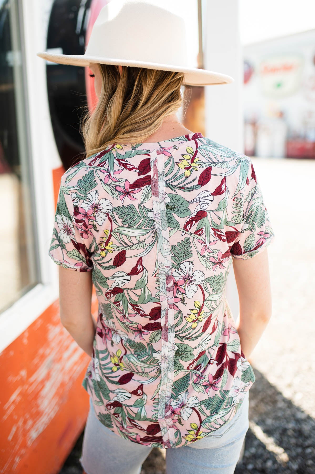Back view of a short sleeve pink floral top that buttons up and has a v-neck.