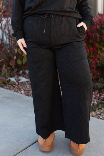 Front view of the pants of the plus size black textured lounge set with pockets and elastic waist