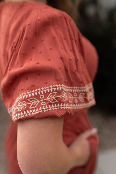 Embroidery detail on the sleeve of a rust dress