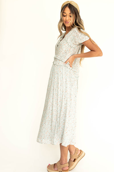 Side view of a light seafoam short sleeve floral dress with ruffle at sleeve.