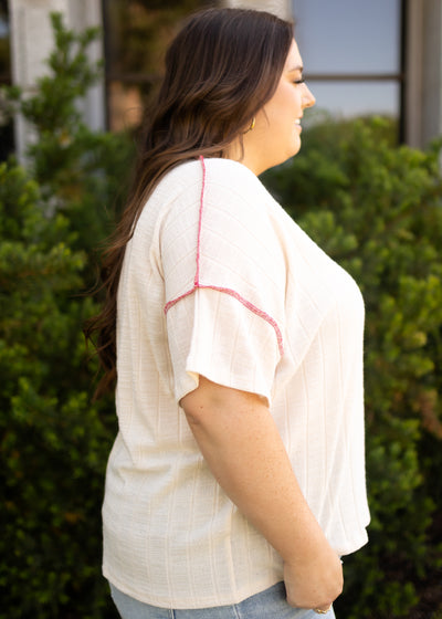 Side view of a short sleeve cream top with coral edging 