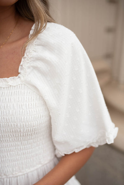 Close up on the neck and sleeve on a white tiered textured dress