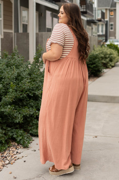 Side view of a plus size clay jumpsuit with pockets