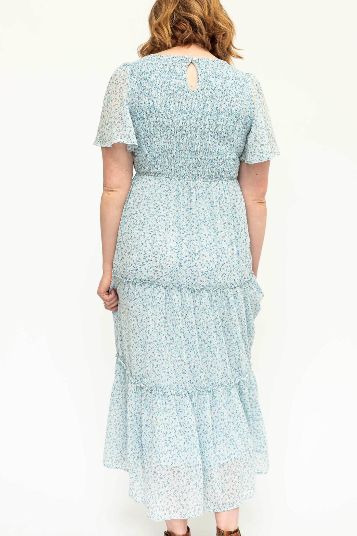 Back view of sky blue sheer fabric with lining, tiered, short sleeve floral dress with smocked bodice.