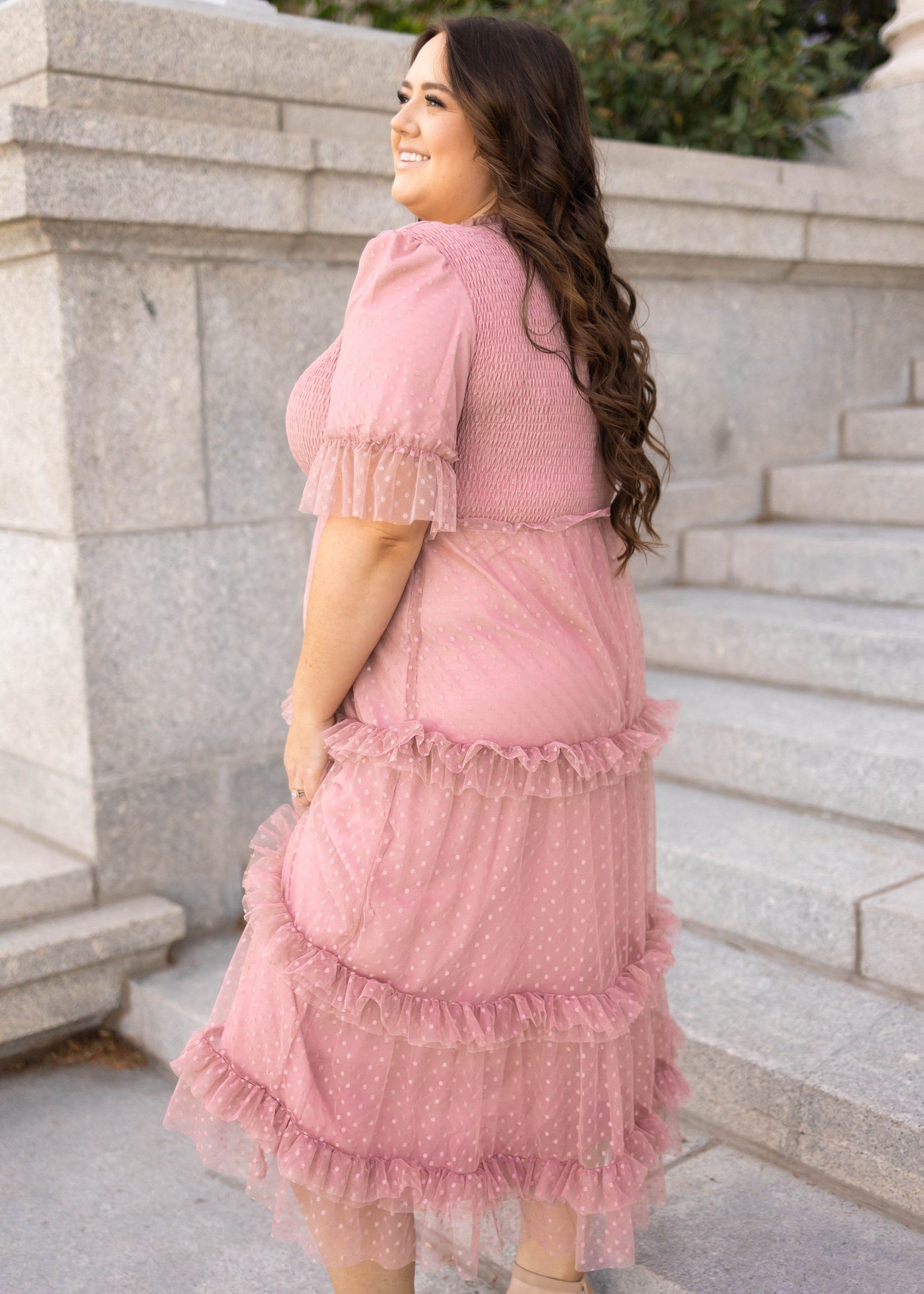 Side view of a dusty pink dress with short sleeves and ruffles on skirt