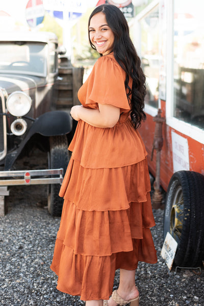Side view of a short sleeve rust colored ruffle dress with elastic waist