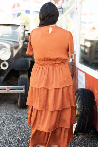 Back view of a short sleeve rust colored ruffle dress with elastic waist