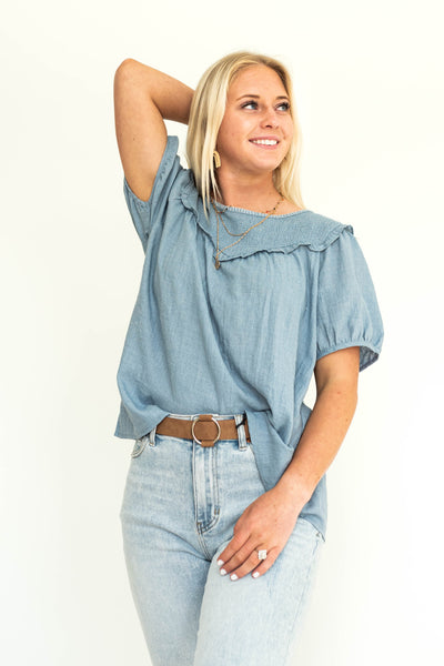 Short sleeve denim chambray blue top with smocking around the neck and ruffle.