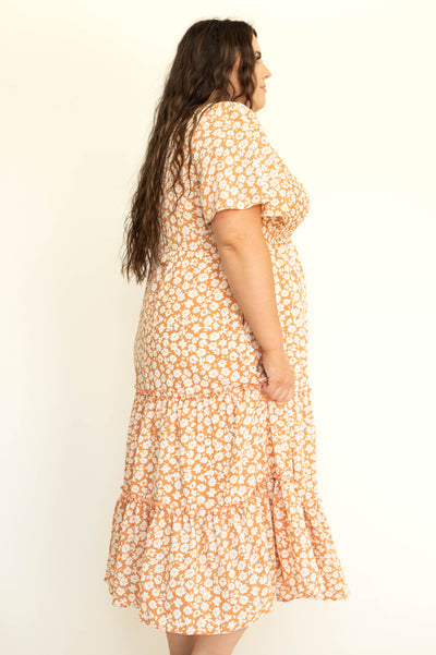 Plus size side view of a short sleeve apricot dress with white flowers and a V-neck.