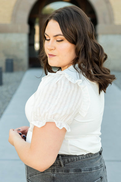 Side view of a plus size short sleeve white top with a ruffle on the sleeve