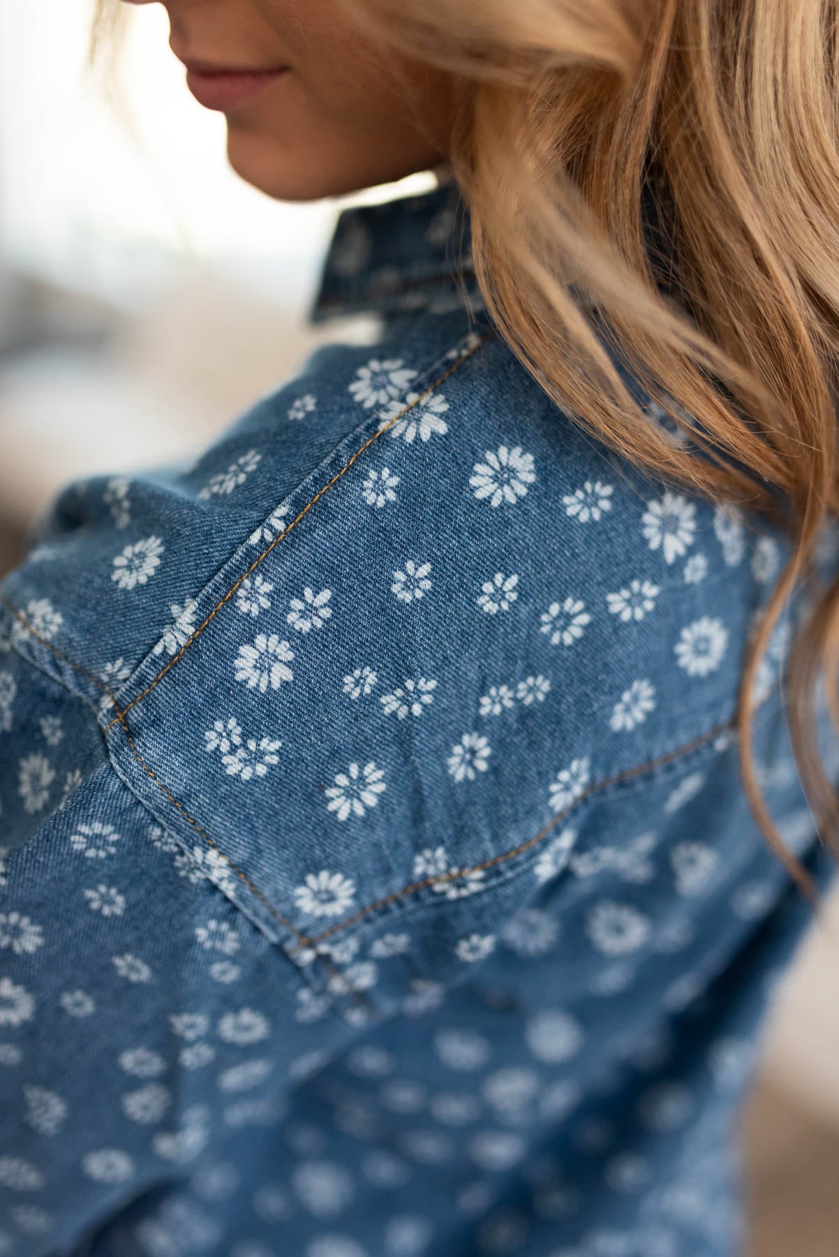 Back view of a denim blue button down top with daisy print