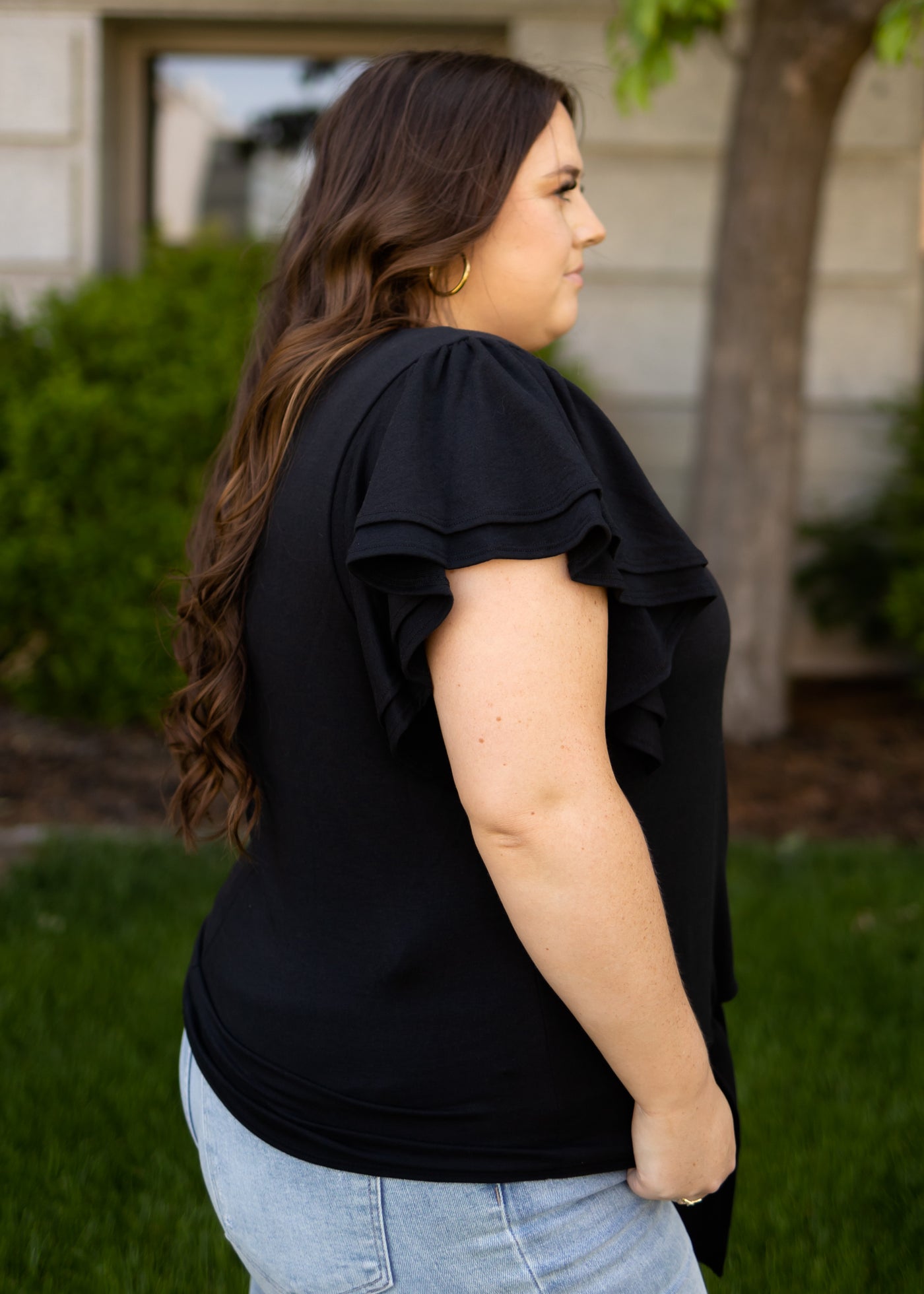 Side view of a plus size black top with short ruffle sleeves