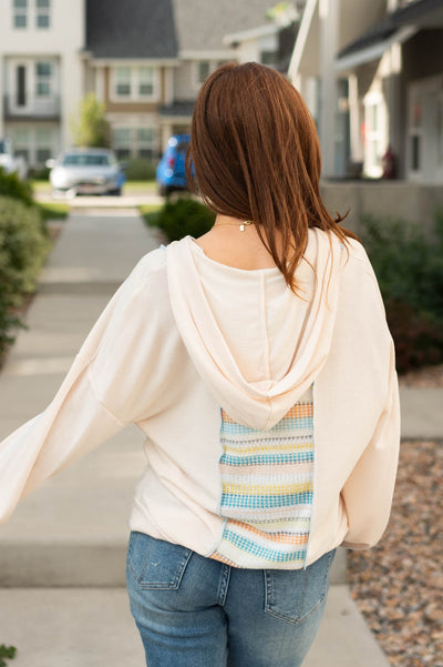 Back view of a oatmeal top with a hood and pastel stripe pattern down the center of the top
