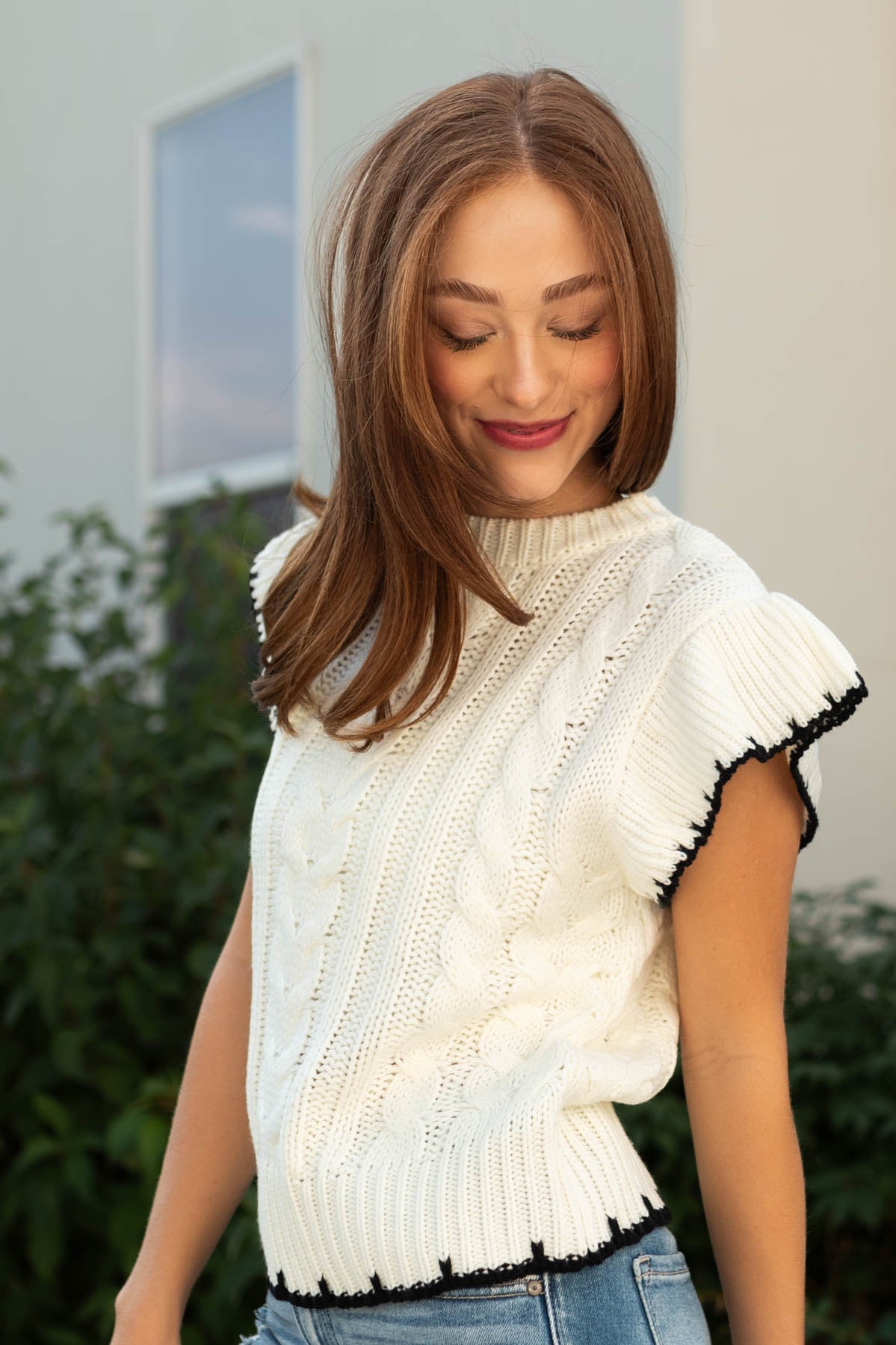 Side view of a ivory knit top with short ruffle sleeves and black edges