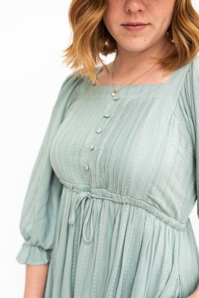 Seafoam green, 3/4 sleeve dress that falls at the waist and has a pleated bodice.
