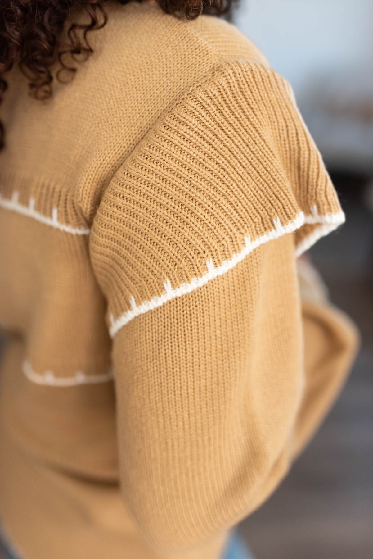 Close up of the ruffle on the sleeve of a taupe stripe sweater