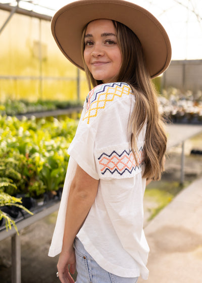 Short sleeve white top with cross stitching pattern on the shoulders and back